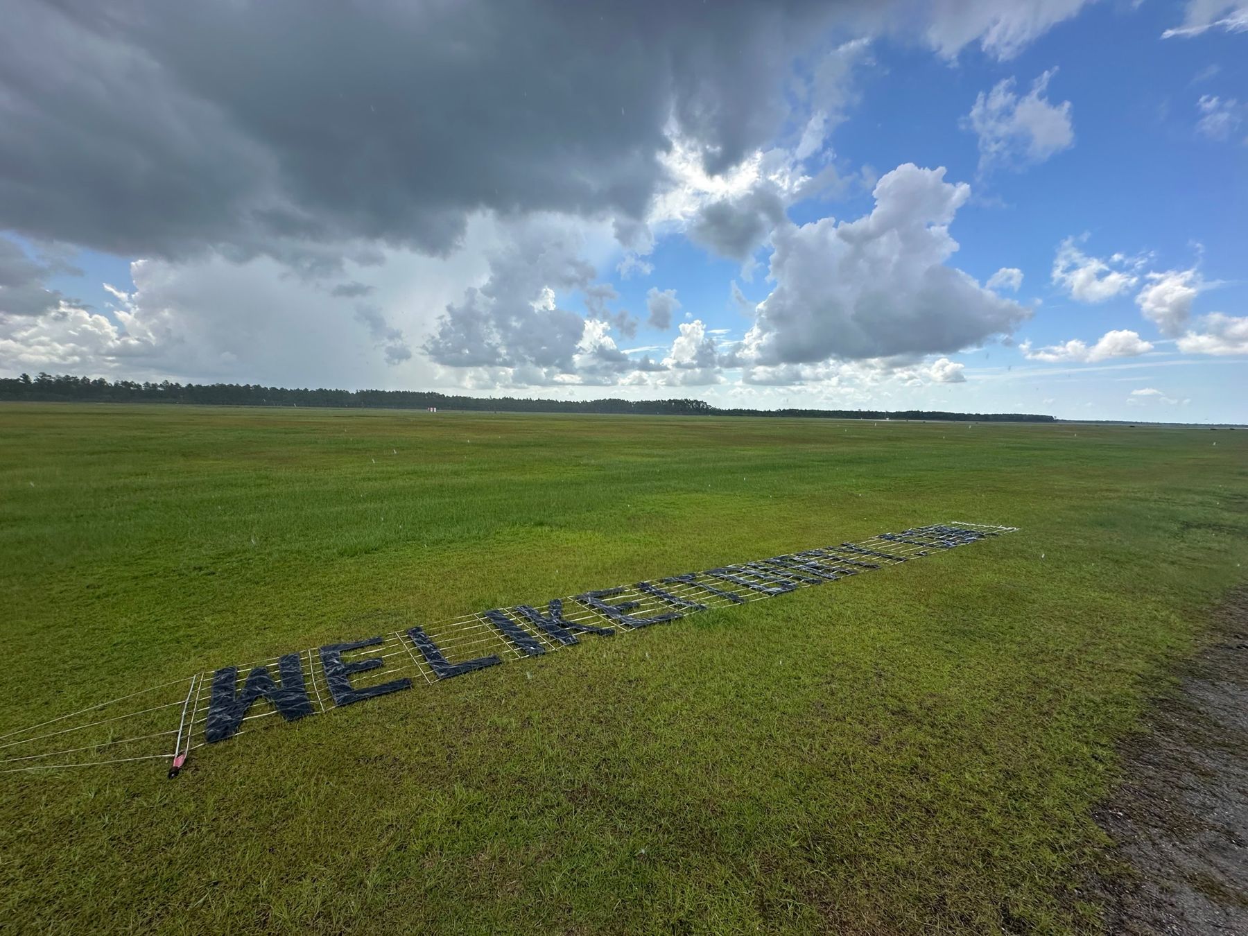 Letter banner laid out on the grass at an airfield before pickup